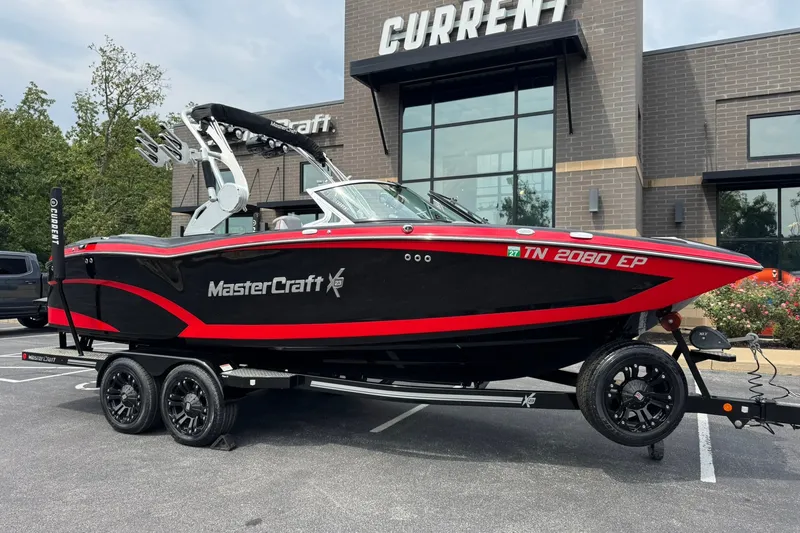 The Image of 2017 MasterCraft X23 boat on trailer, parked outside a modern building. - 1