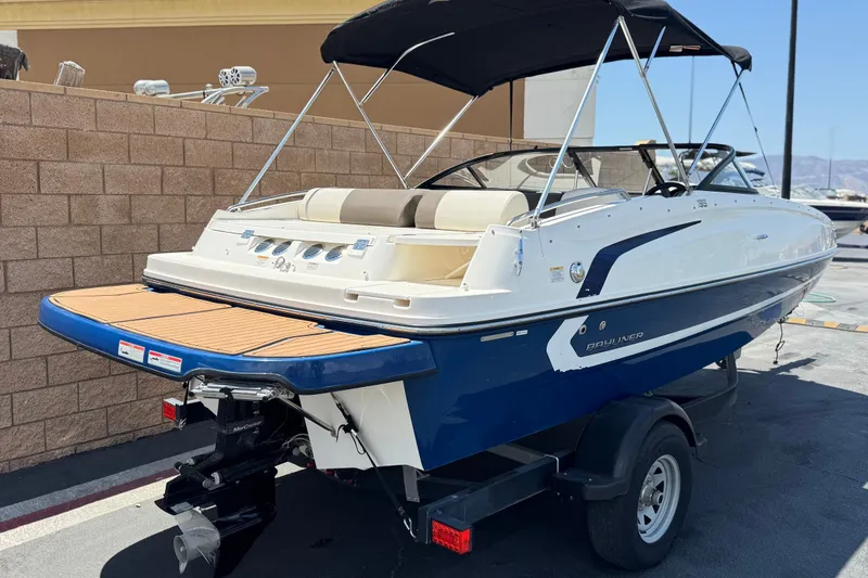 Slide: The Image of 2019 Bayliner 195 Deck Boat with blue and white exterior, parked on a trailer. - 5