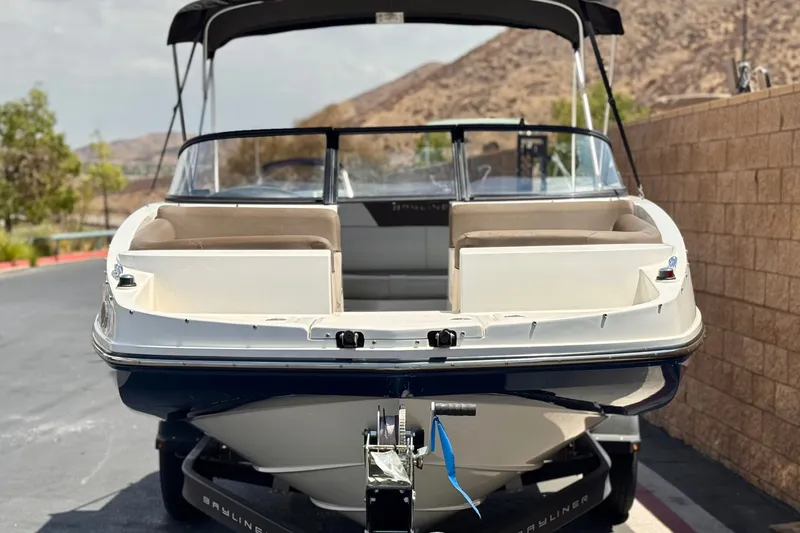 Slide: The Image of 2019 Bayliner 195 Deck Boat with canopy, parked on a trailer, scenic background. - 2