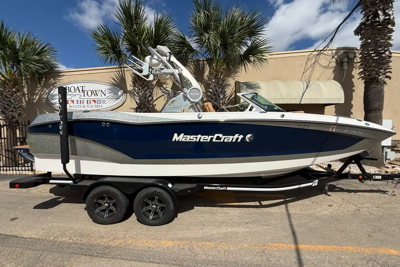 The Image of 2020 MasterCraft X24 boat on trailer, parked outdoors with palm trees in background. - 1