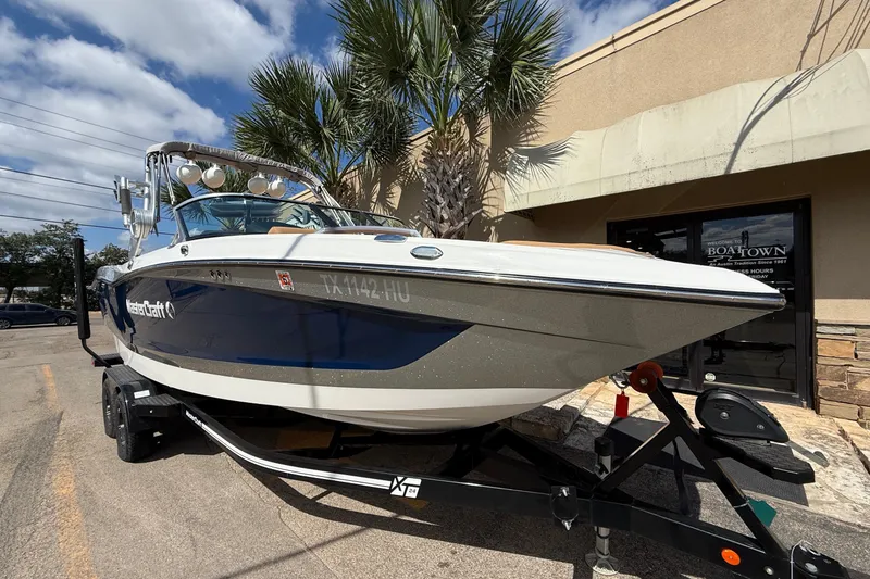 Slide: The Image of 2020 MasterCraft X24 boat on trailer, parked outside a building under a clear sky. - 2