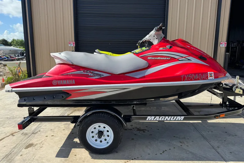 The Image of 2006 Yamaha WaveRunner VX110 Deluxe in red on a trailer, parked outside a garage. - 1