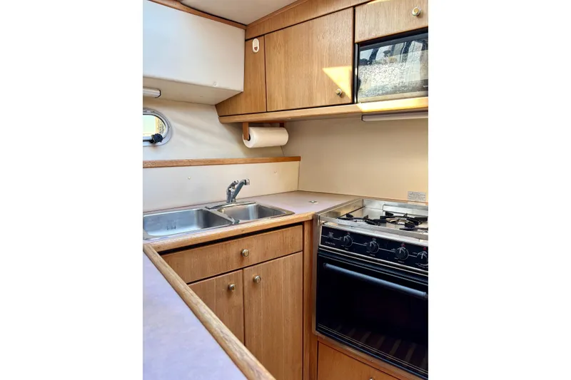 Slide: The Image of 1998 Bayliner 3388 Command Bridge Motoryacht kitchen with stove, sink, and wooden cabinets. - 25