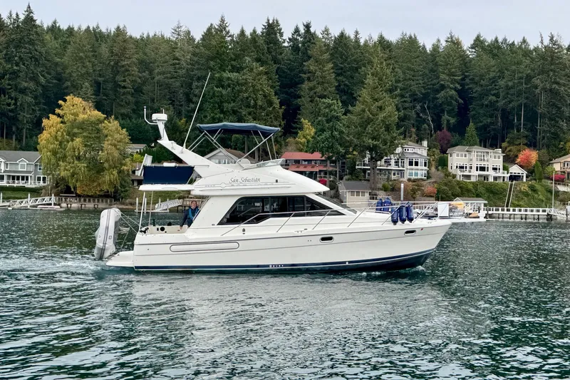 Slide: The Image of 1998 Bayliner 3388 Command Bridge Motoryacht cruising near waterfront homes and lush forest. - 47