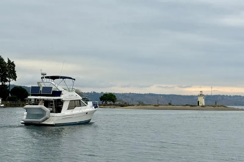 Slide: The Image of 1998 Bayliner 3388 Command Bridge Motoryacht cruising near a lighthouse on a cloudy day. - 48