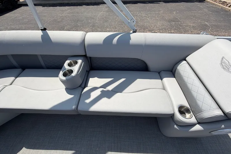 Slide: The Image of 2025 Bennington 22 L Quad Bench with gray upholstery and cup holders on a sunny day. - 26