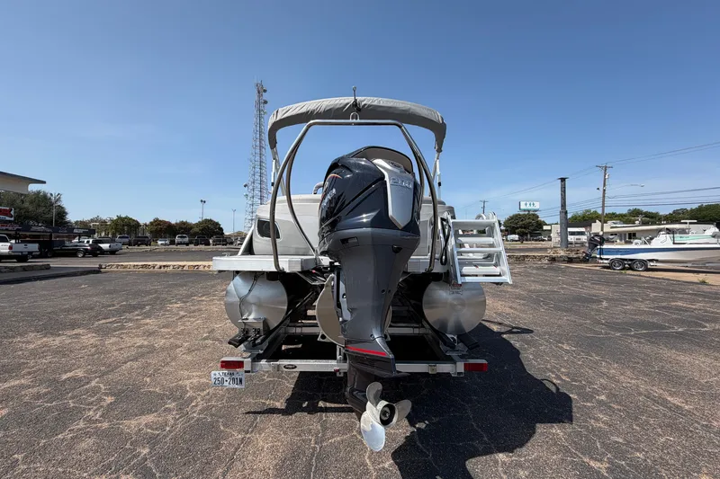 Slide: The Image of 2025 Bennington 22 L Quad Bench pontoon boat with outboard motor, parked on asphalt. - 3