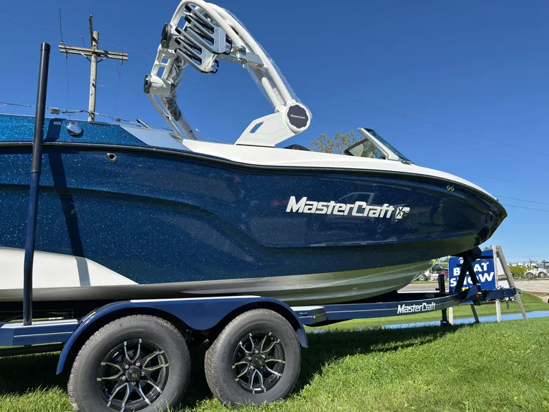 Slide: The Image of A 2027 MasterCraft XT22 boat on a trailer, set on green grass under a blue sky. - 7
