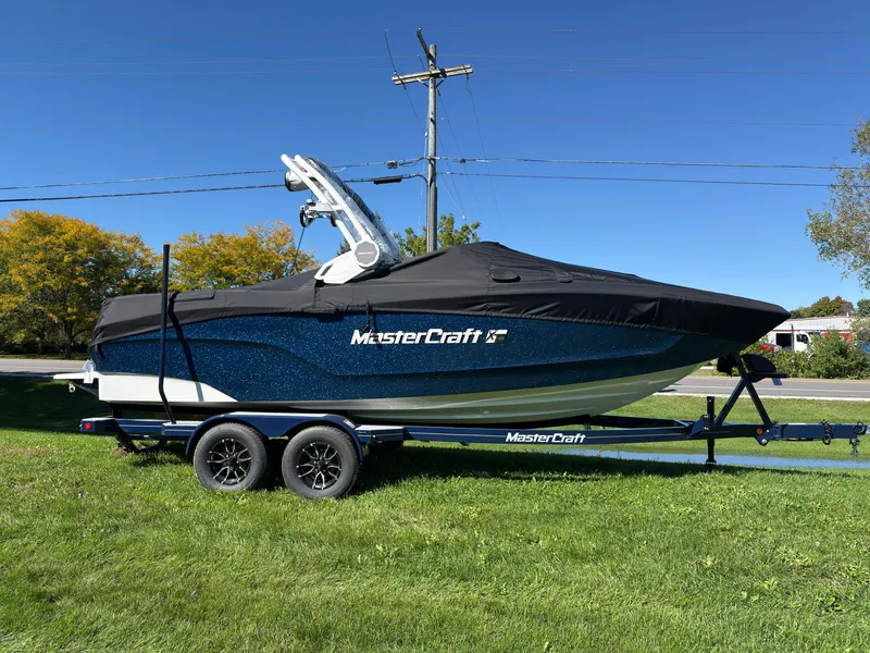 Slide: The Image of A 2027 MasterCraft XT22 boat on a trailer, parked on grass. - 1