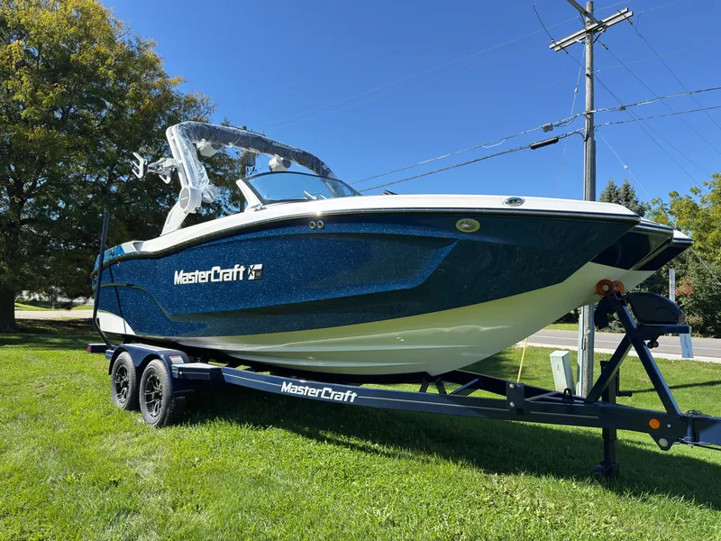 Slide: The Image of A 2027 MasterCraft XT22 boat on a trailer, set on a green lawn. - 2