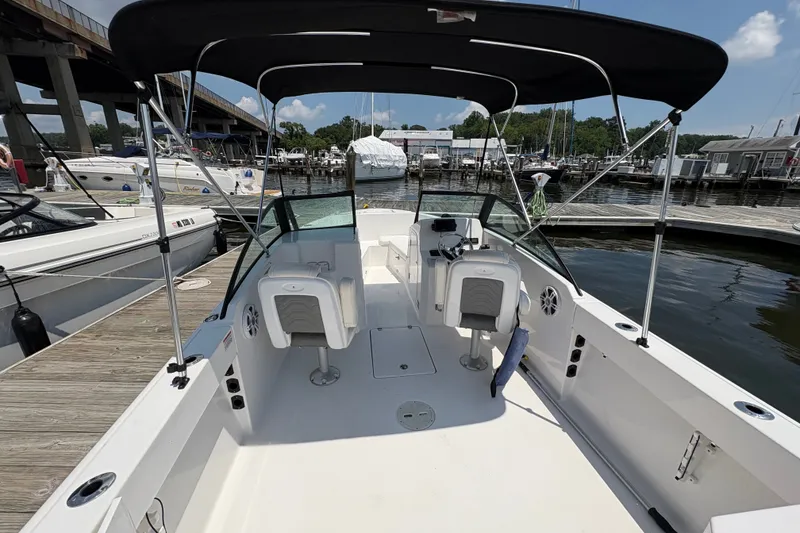 Slide: The Image of 2024 Aquasport 2200 Dual Console boat docked at marina, featuring spacious seating and canopy. - 7