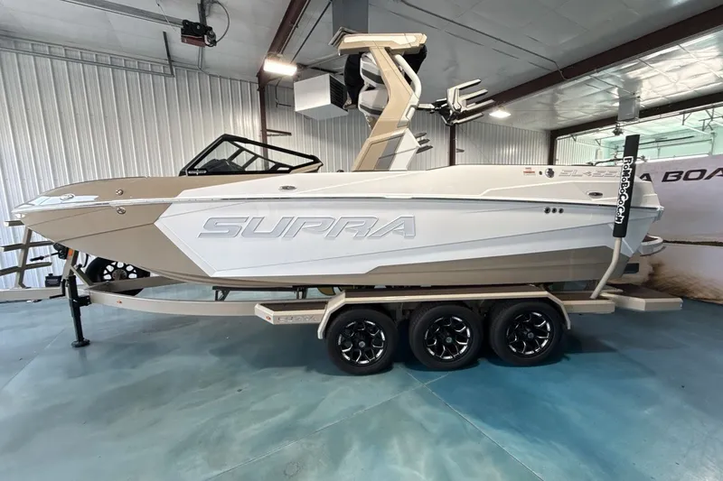 Slide: The Image of 2027 Supra SL 550 boat in showroom, featuring sleek design and triple-axle trailer. - 38