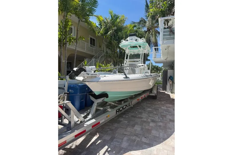 Slide: The Image of 2023 Caymas 281 HB boat on trailer, parked near tropical trees and a house. - 6
