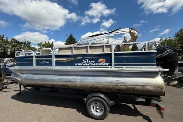 The Image of 2024 Sun Tracker Bass Buggy 18 DLX pontoon boat on trailer under blue sky. - 1