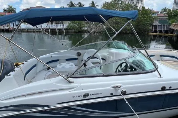 Slide: The Image of 2013 Hurricane SunDeck 2400 OB boat with blue canopy, docked near waterfront homes. - 2