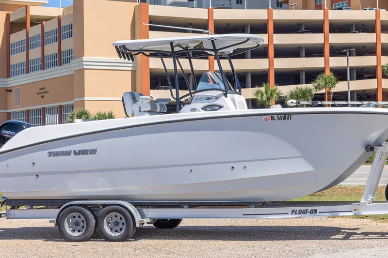 The Image of 2022 Twin Vee 240 GFX CC boat on trailer, parked near a multi-story building. - 0