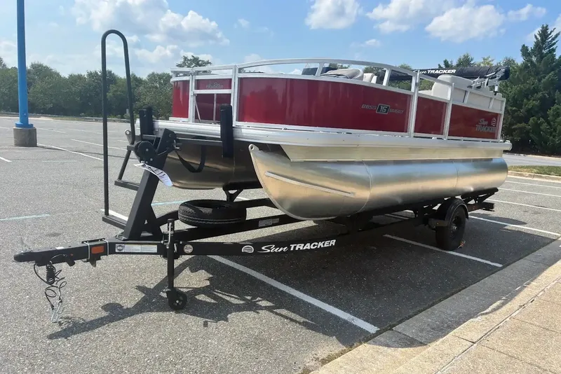 The Image of 2026 Sun Tracker Bass Buggy 16 XL Select pontoon boat on trailer in parking lot. - 0