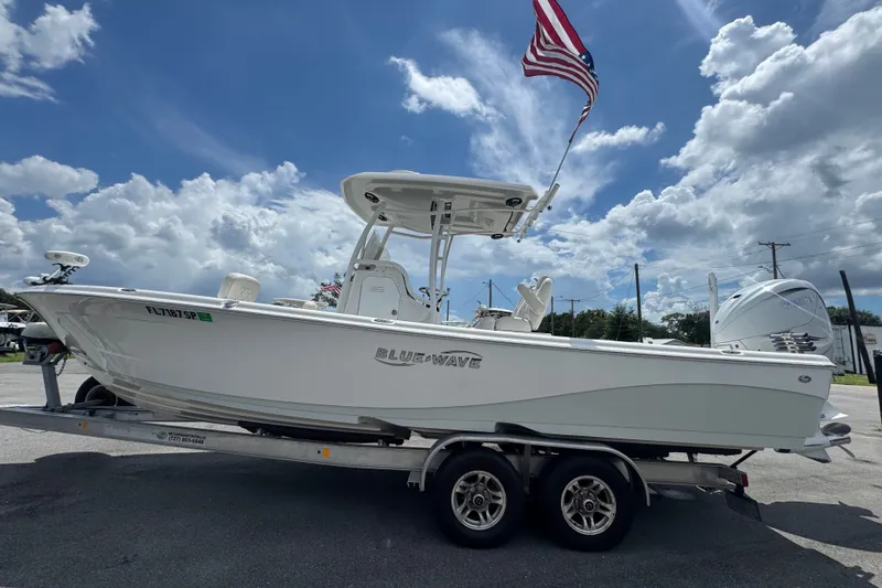 The Image of 2019 Blue Wave 2800 Pure Hybrid boat on trailer with American flag, under cloudy sky. - 0