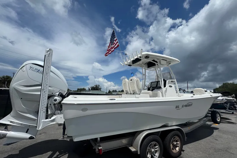 Slide: The Image of 2019 Blue Wave 2800 Pure Hybrid boat on trailer, under cloudy sky with American flag. - 16