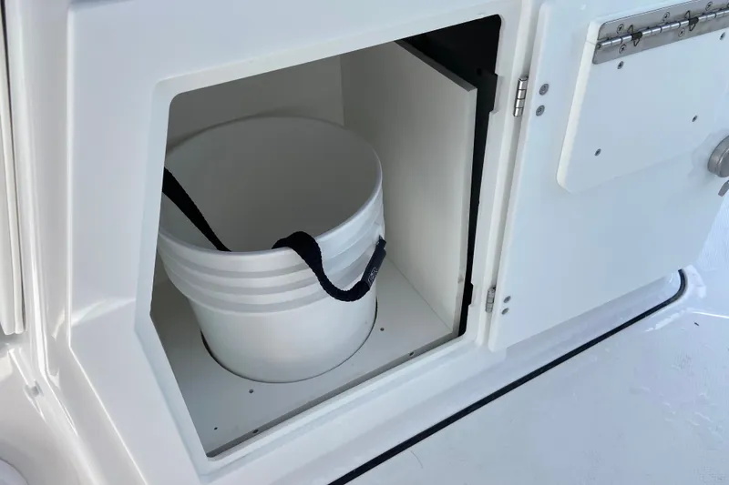 Slide: The Image of Storage compartment with a white bucket inside the 2027 Monterey Elite 30 OB boat. - 16