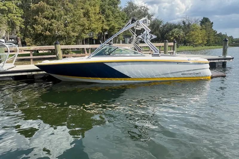 The Image of 2007 MasterCraft X-15 SS boat docked on a calm lake with trees in the background. - 0