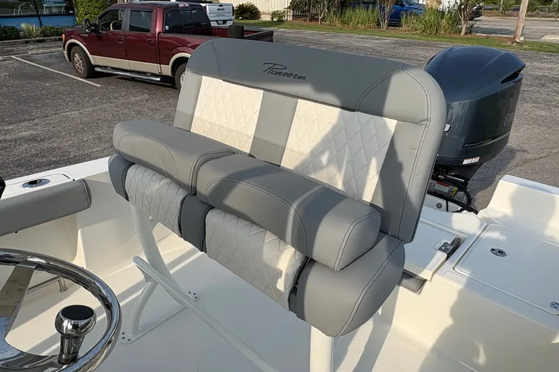 Slide: The Image of 2027 Pioneer 220 Bay Sport boat with cushioned seating and outboard motor in a parking lot. - 17