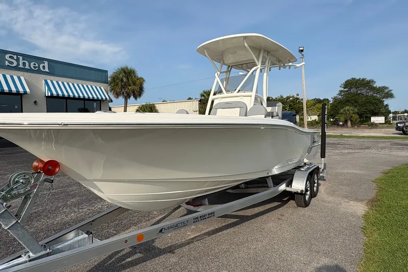 Slide: The Image of 2027 Pioneer 220 Bay Sport boat on trailer, parked outside a building with blue-striped awnings. - 6