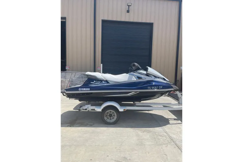 The Image of 2016 Yamaha VX-Deluxe jet ski on trailer outside a garage. - 0