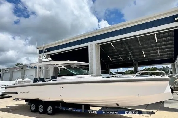 Slide: The Image of 2024 Axopar 37 Sun-Top boat on trailer, parked outside a dealership under a cloudy sky. - 9