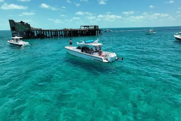 Slide: The Image of 2024 Axopar 37 Sun-Top boat cruising near a shipwreck in clear turquoise waters. - 14