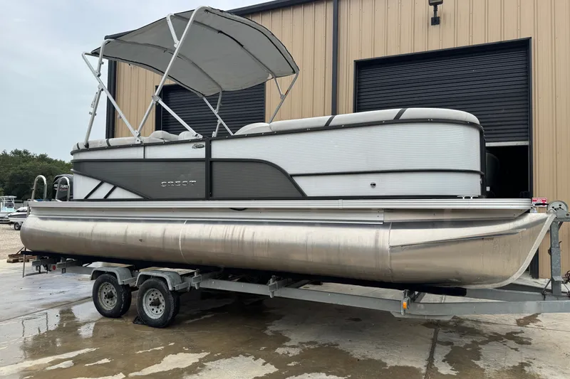 Slide: The Image of 2023 Crest 220 Classic LX pontoon boat on trailer outside a warehouse. - 2