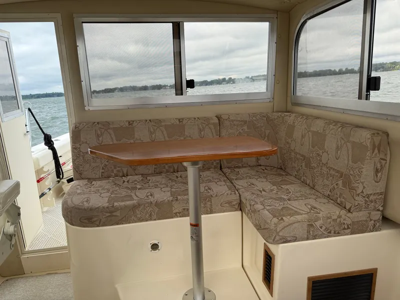 Slide: The Image of Interior of a 2008 Shamrock 270 Mackinaw with cushioned seating and a wooden table, surrounded by windows. - 11