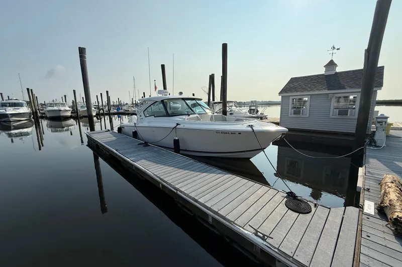 Slide: The Image of 2026 Pursuit DC 326 Dual Console boat docked at a marina on a sunny day. - 2