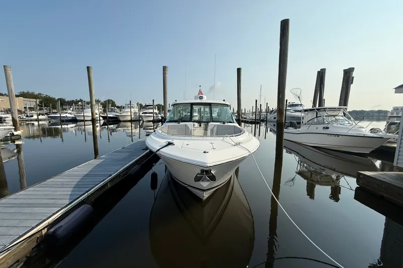 Slide: The Image of 2026 Pursuit DC 326 Dual Console boat docked at a marina, surrounded by calm waters. - 1