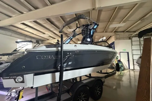 Slide: The Image of 2023 Cobalt R4 Surf boat in showroom, sleek design, gray and white exterior. - 2