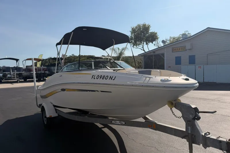 Slide: The Image of 2006 Sea Ray 185 Sport boat on trailer with canopy, parked near a building. - 2