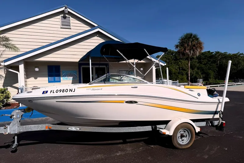 Slide: The Image of 2006 Sea Ray 185 Sport boat on trailer, parked near a building with palm trees. - 0