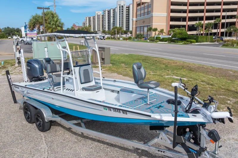 Slide: The Image of 2024 Xpress H22 Bay boat on trailer, parked near a road with buildings in background. - 2