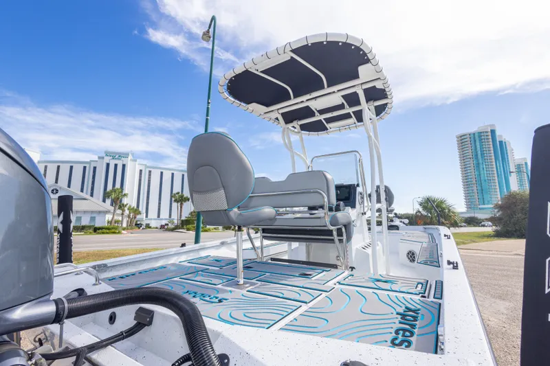 Slide: The Image of 2024 Xpress H22 Bay boat with T-top, parked near modern buildings. - 50