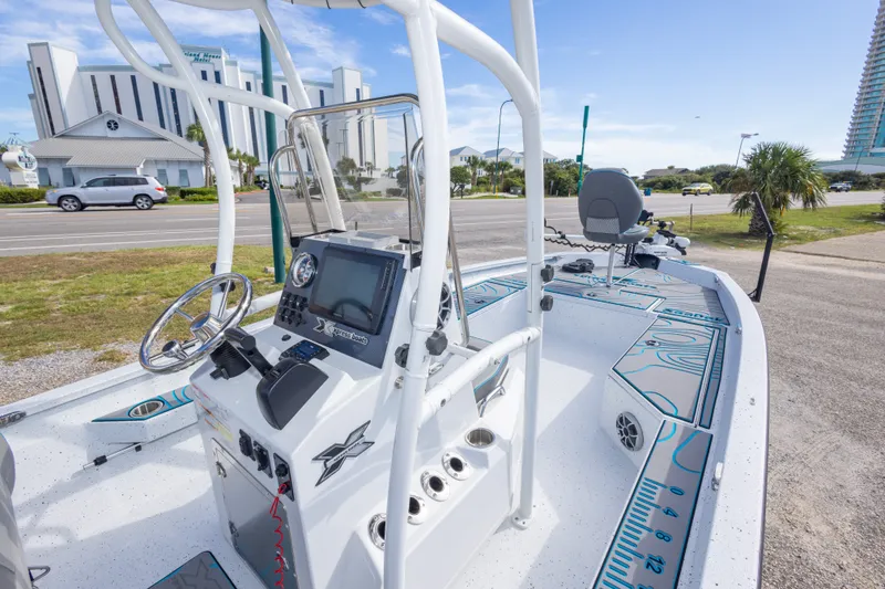Slide: The Image of 2024 Xpress H22 Bay boat with modern console and seating, parked near a coastal road. - 27