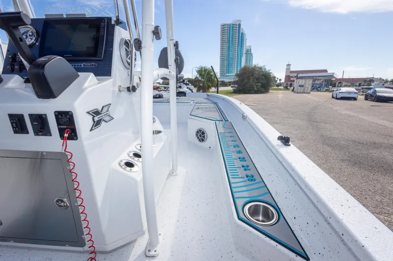 Slide: The Image of 2024 Xpress H22 Bay boat interior with console and measuring ruler, parked near buildings. - 47