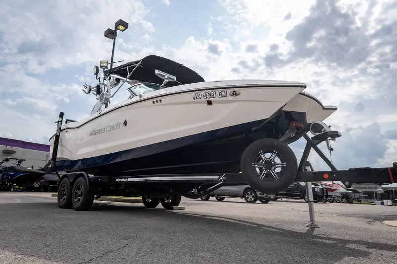 Slide: The Image of 2021 MasterCraft X24 boat on trailer under cloudy sky at dealership. - 58
