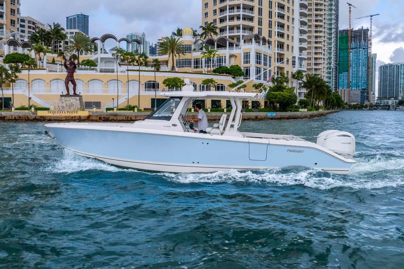 Slide: The Image of 2025 Pursuit S 328 Sport boat cruising near waterfront buildings and statue. - 2