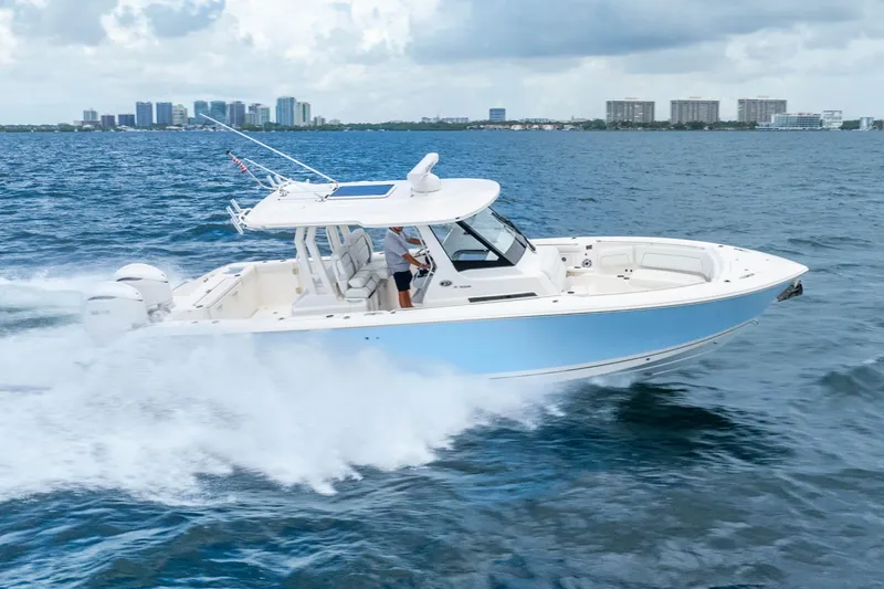 Slide: The Image of 2025 Pursuit S 328 Sport boat cruising on open water with city skyline backdrop. - 5
