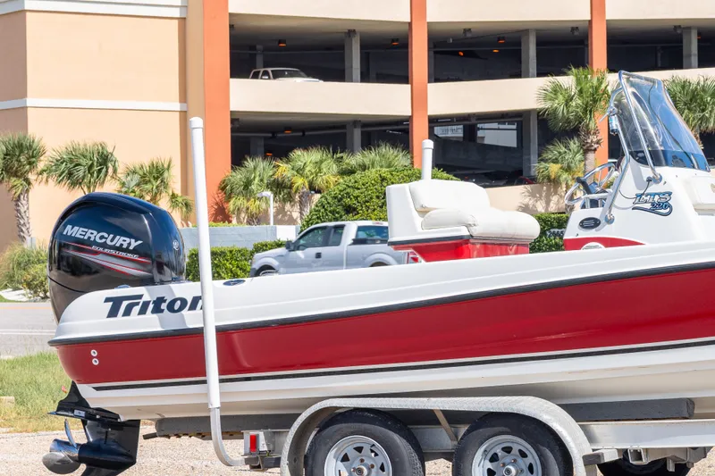 Slide: The Image of 2003 Triton 220 LTS boat with Mercury engine, parked near a building and greenery. - 10