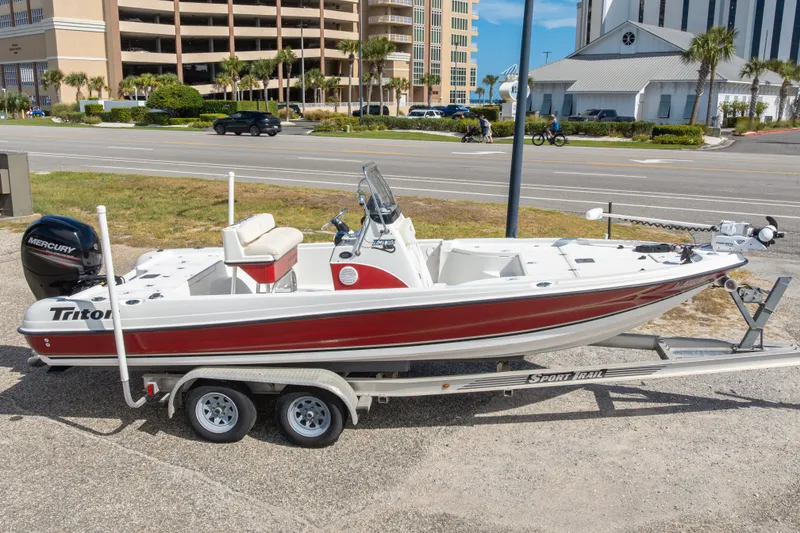Slide: The Image of 2003 Triton 220 LTS boat on trailer, parked near road with buildings in background. - 2