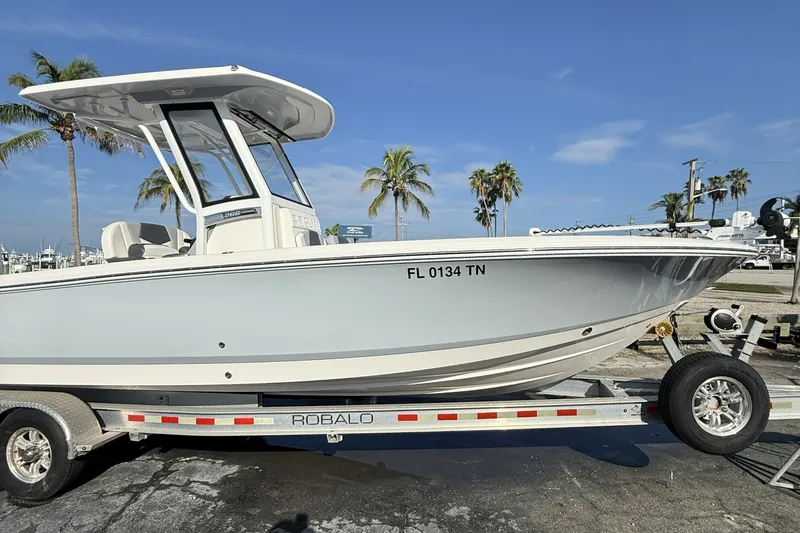 Slide: The Image of 2023 Robalo 266 Cayman boat on trailer, parked near palm trees under clear blue sky. - 3