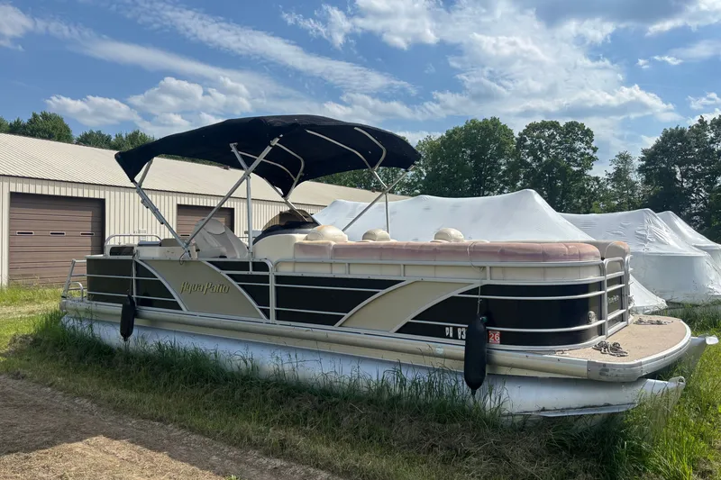Slide: The Image of 2011 AquaPatio AP250W6 pontoon boat with canopy, parked outdoors near storage buildings. - 2
