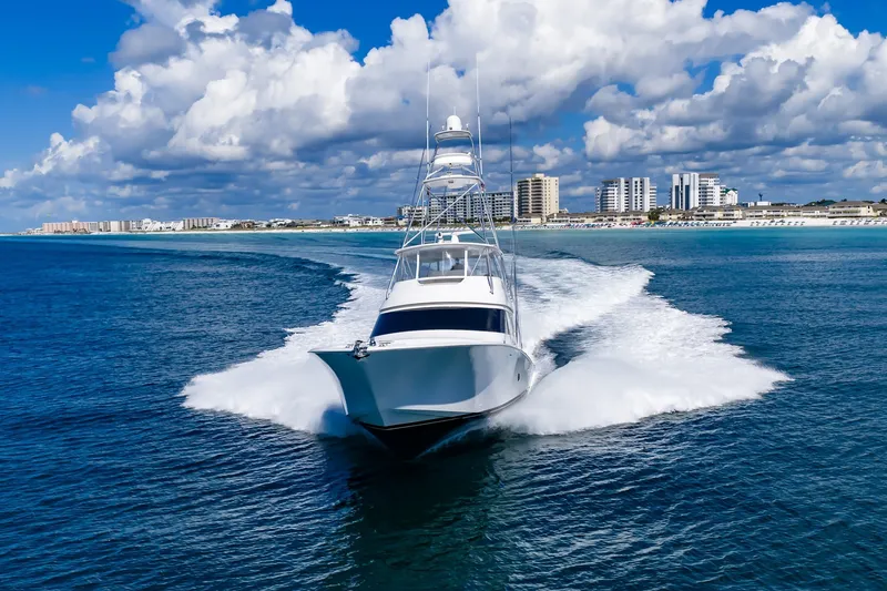 Slide: The Image of 2012 Viking 76 Convertible yacht cruising near a coastal city under a blue sky. - 21