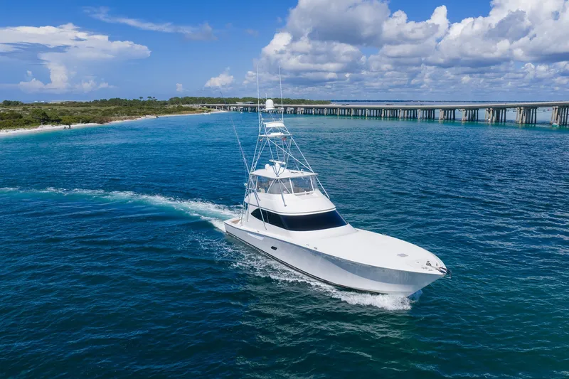 Slide: The Image of 2012 Viking 76 Convertible yacht cruising on blue ocean near a bridge under a cloudy sky. - 10
